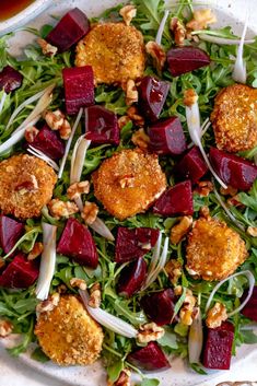 a salad with beets, carrots and nuts on a white plate next to a cup of tea