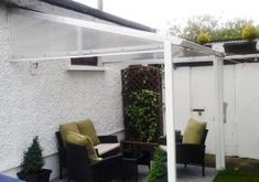 a patio area with chairs and plants on the side of the house that is covered by a pergolated roof