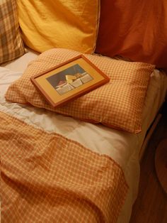 a bed with orange and yellow pillows and a framed picture on the pillow case next to it