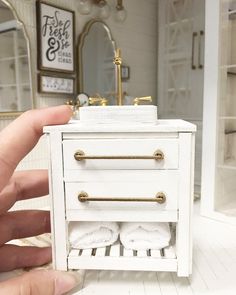 someone is holding up a miniature white cabinet with gold handles and knobs on it