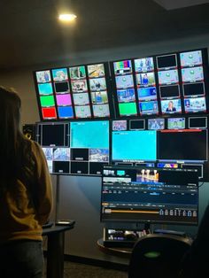 a woman standing in front of two monitors with multiple screens on the wall behind her