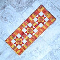 an orange and yellow quilt laying on the floor next to a white tiled flooring