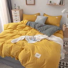 a bed with yellow sheets and pillows in a room next to a white wall,