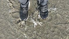 a person standing in shallow water wearing black shoes