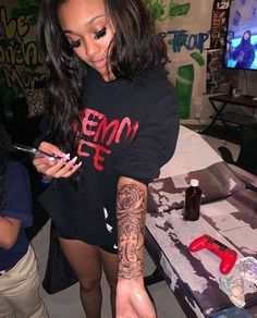 a woman with tattoos on her arm holding a cell phone and looking at the screen