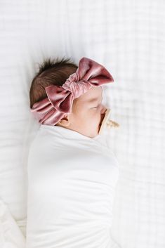 a baby with a pink bow laying on top of a white blanket in the bed