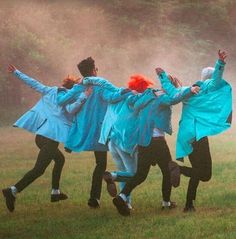 a group of people jumping in the air on top of a grass covered field with trees behind them