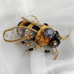 a yellow and black insect sitting on top of a white cloth covered table next to a piece of jewelry