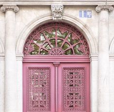 an ornately designed pink double door on a white building with stone pillars and arches