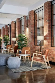 an empty lobby with chairs and tables in front of large windows, brick walls and floor to ceiling windows