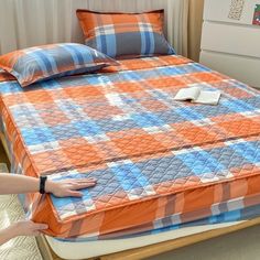 an orange and blue checkered bedspread on a bed with two hands reaching for it