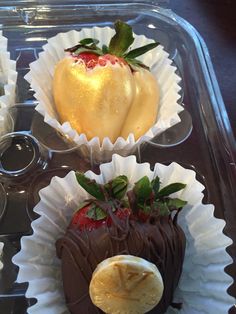 three chocolate covered strawberries in paper cups on a tray with other desserts and condiments