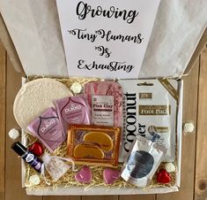 an open gift box filled with various types of food and condiments, along with a sign that says growing tiny humans is exhausting