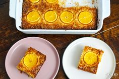 two plates with orange slices on them next to a casserole dish filled with baked goods