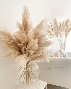 a vase filled with dry grass sitting on top of a white table next to a couch