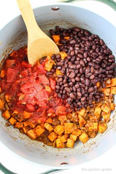 beans, tomatoes and other ingredients are mixed together in a white bowl with a wooden spoon