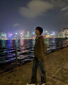 a man is standing on a skateboard by the water at night with city lights in the background