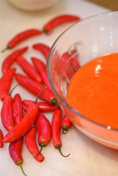 some red hot peppers on a white cutting board next to a bowl of orange sauce