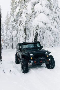 a jeep driving through the snow in front of trees