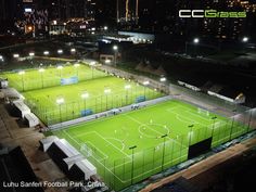 an aerial view of a soccer field at night with the lights on and buildings in the background