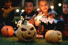 three children sitting on the grass with halloween decorations and sparklers in front of them