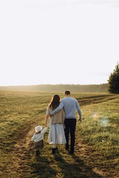 a man and woman walking down a dirt road with a small child on the other side