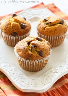 three chocolate chip muffins on a white plate with an orange towel in the background