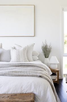 a bed with white sheets and pillows in a bedroom next to a painting on the wall