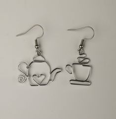 a pair of silver earrings with a teapot and heart on it, hanging from hooks