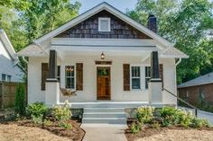 a small white house with brown shutters on the front door and steps leading up to it