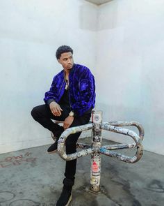 a man sitting on top of a chair made out of pipes and chains with his legs crossed