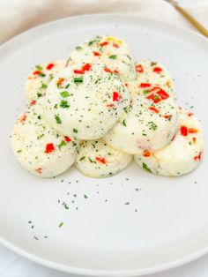 some food is on a white plate with green sprinkles and red peppers