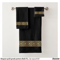 two black towels with gold greek design hanging on a towel rack in front of a white wall