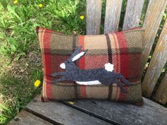 a plaid pillow with a rabbit on it sitting on a wooden bench in the grass