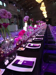 the long table is set with purple flowers and place settings for guests to sit at