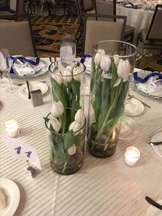 two vases filled with white tulips on top of a dining room table