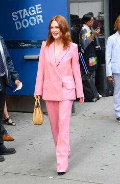 a woman in a pink suit is walking down the street with her hand on her hip