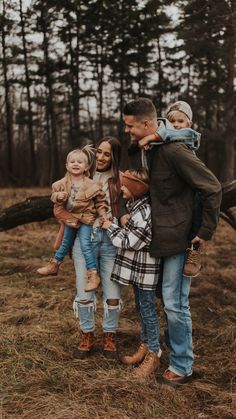 a group of people standing in the woods with one holding two small children and looking into the distance