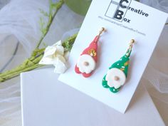 two christmas themed earrings sitting on top of a white table next to flowers and a card