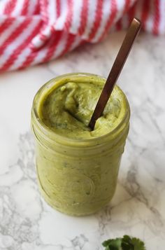 a jar filled with green sauce sitting on top of a counter next to a wooden spoon