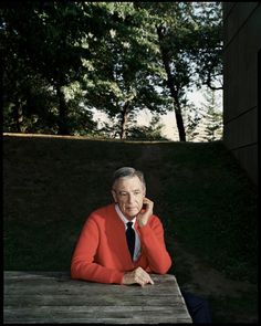 an older man sitting at a table talking on a cell phone while wearing a red sweater and black tie