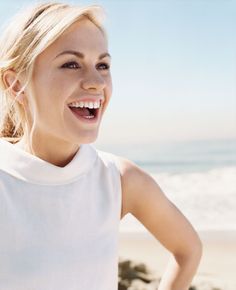 a woman standing on the beach with her hands on her hips and smiling at the camera