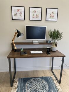 a wooden desk with a computer monitor and keyboard sitting on top of it next to two framed pictures