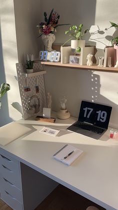 a white desk topped with a laptop computer next to a shelf filled with plants and candles