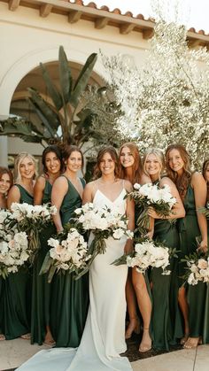 a group of women standing next to each other holding bouquets in front of a building