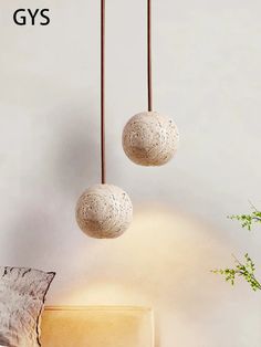 two white balls hanging from the ceiling next to a chair and plant in a vase