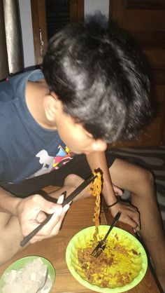 a young man is eating noodles from a yellow plate