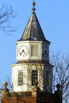 a large clock tower on top of a building with trees in the foreground and blue sky behind it