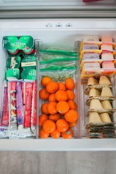 an open refrigerator filled with oranges, yogurt and other food items in plastic containers