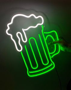 a neon beer sign is lit up with green and white lights in the shape of a mug